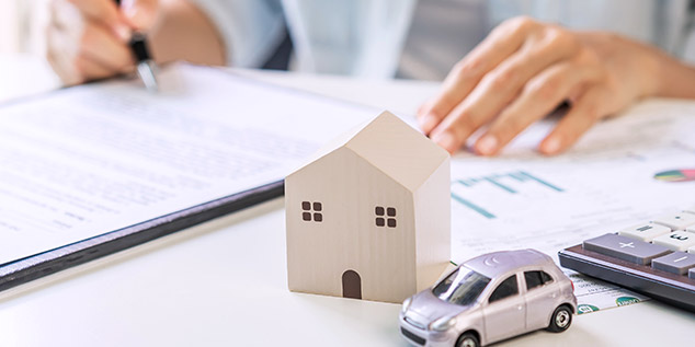 Una casa y un coche en miniatura mientras una mujer escribe